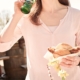 Eine Frau mit Sonnenbrille lächelt, hält ein Sandwich in der Hand und trinkt an einem sonnigen Tag im Freien aus einer grünen Glasflasche.