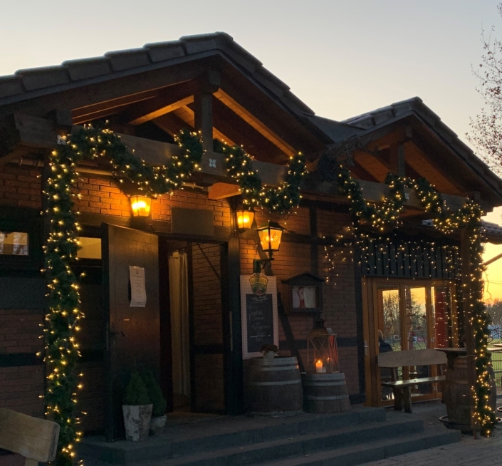 Eingang Flürchen Weihnachtsbeleuchtung close Ein gemütliches Gebäude, das bei Sonnenuntergang mit Weihnachtslichtern und Girlanden geschmückt ist und am Eingang warme Lichter leuchten.