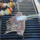 Eine Person grillt Lammkarree, Gemüsespieße und Würstchen auf einem Grill im Freien.