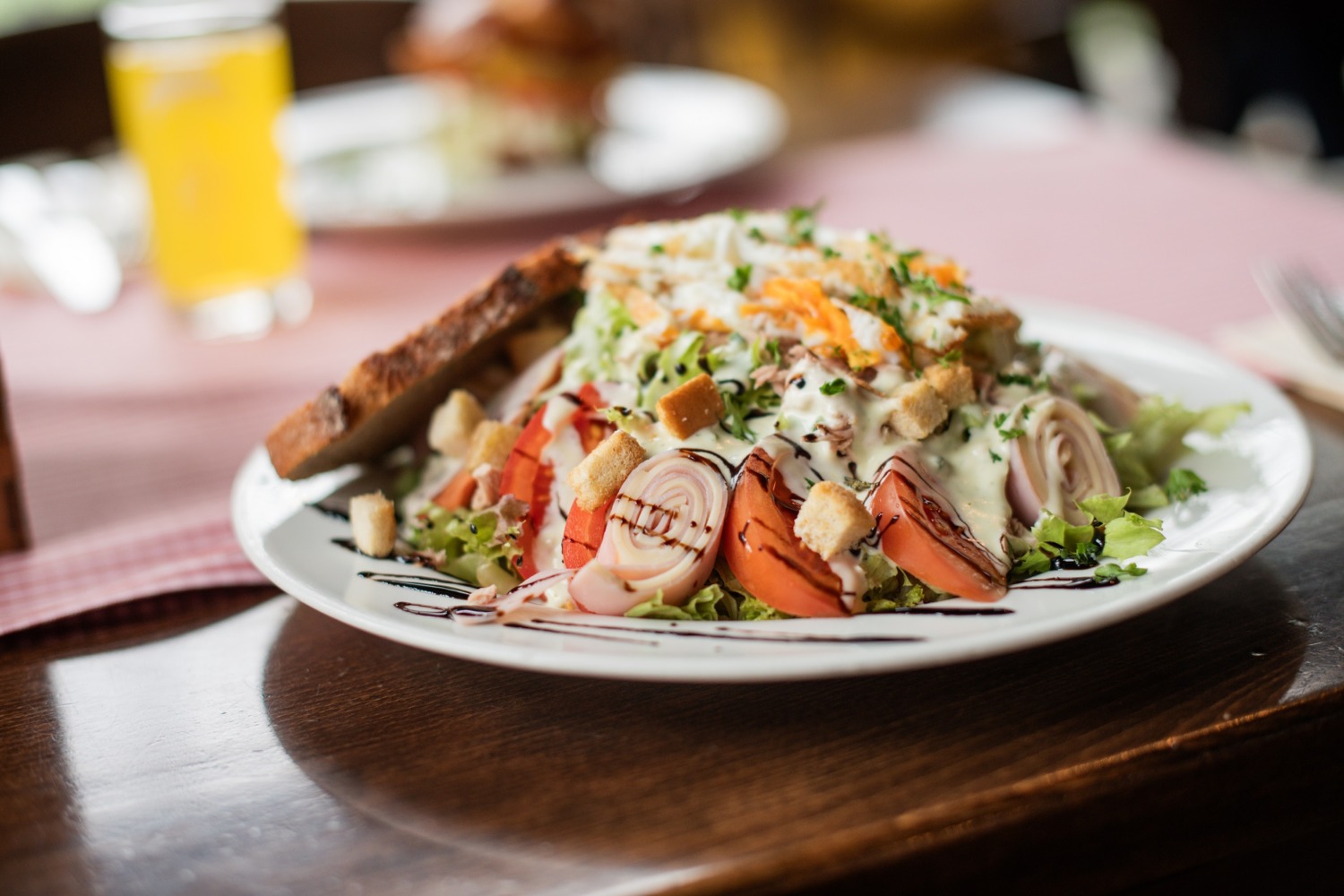 Ein Salatteller mit gerolltem Fleisch, Tomaten, Croutons, geriebenem Käse, Dressing und einer Scheibe getoastetem Brot als Beilage.