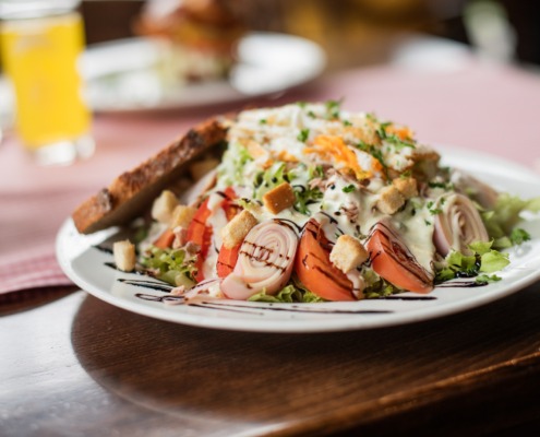 Ein Salatteller mit gerolltem Fleisch, Tomaten, Croutons, geriebenem Käse, Dressing und einer Scheibe getoastetem Brot als Beilage.