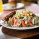 Ein Salatteller mit gerolltem Fleisch, Tomaten, Croutons, geriebenem Käse, Dressing und einer Scheibe getoastetem Brot als Beilage.