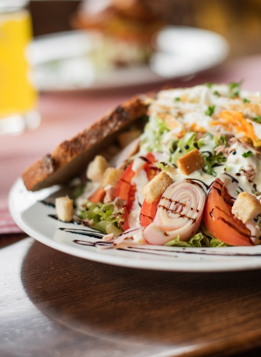 Ein Salatteller mit gerolltem Fleisch, Tomaten, Croutons, geriebenem Käse, Dressing und einer Scheibe getoastetem Brot als Beilage.